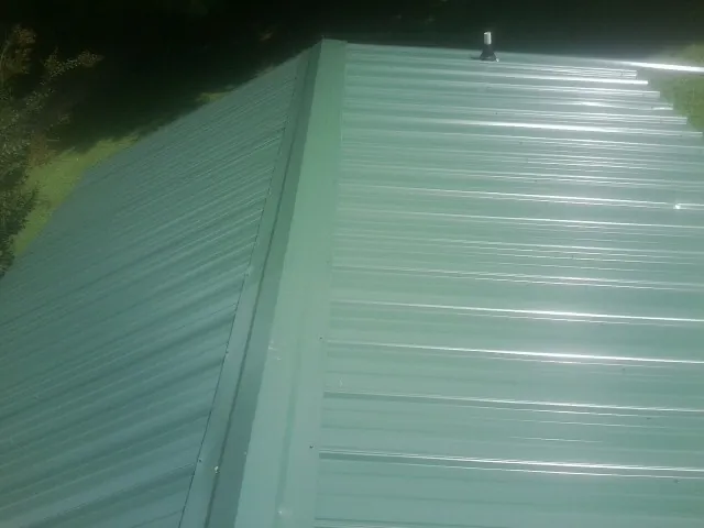 New green metal panels meeting at the ridge of a roof — Flat Roof Repair work by our crew in Millbrook